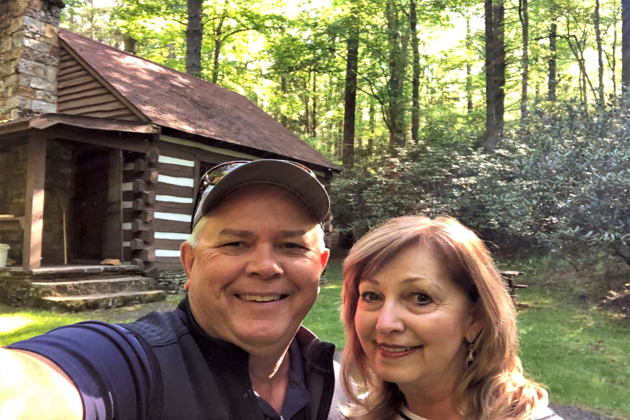 All smiles are Ken and Judy Caplinger as they pose for a selfie making memories t Watoga State Park, Cabin No. 34, also known as the Honeymoon Cabin. The log cabin is in the background surround by a lush forest and mountain laurel that is common through West Virginia's largest state park.