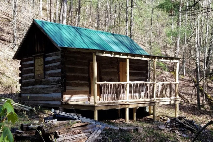 Volunteers at Watoga are nearing completion of restorative efforts on the Workman-Jarvis Cabin. It's in a wooded setting with a green metal roof. Hand-hewn rails line the new porch. Photo by the Watoga State Park Foundation.